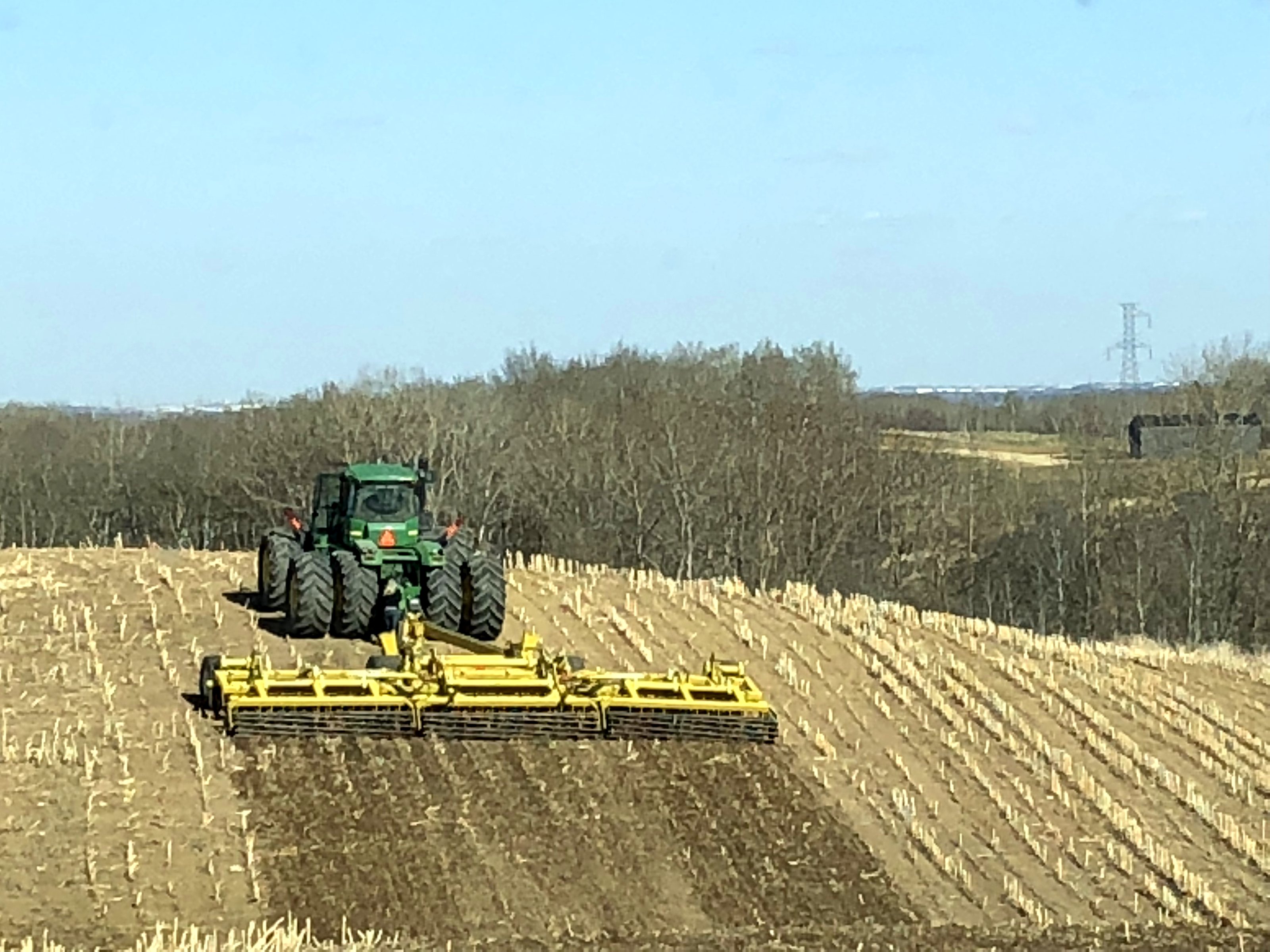 A John Deere tractor pulling harrows across stubble in spring