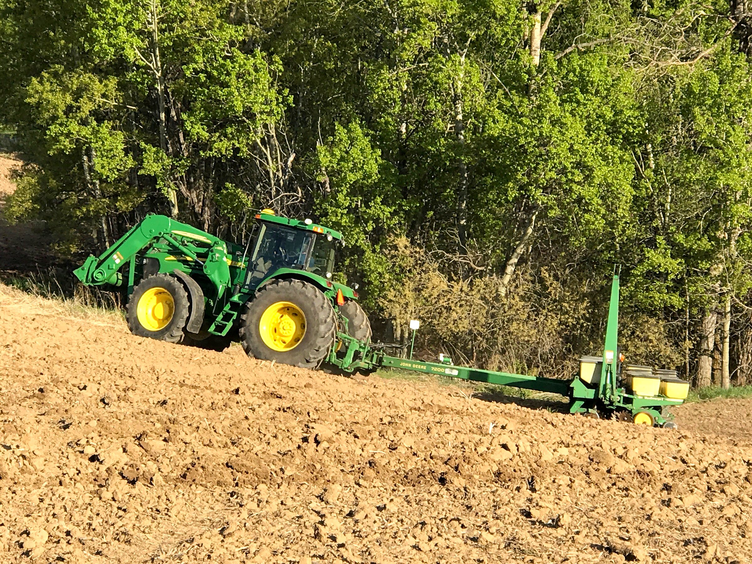 A John Deere tractor and planter, wings folded, at the treeline