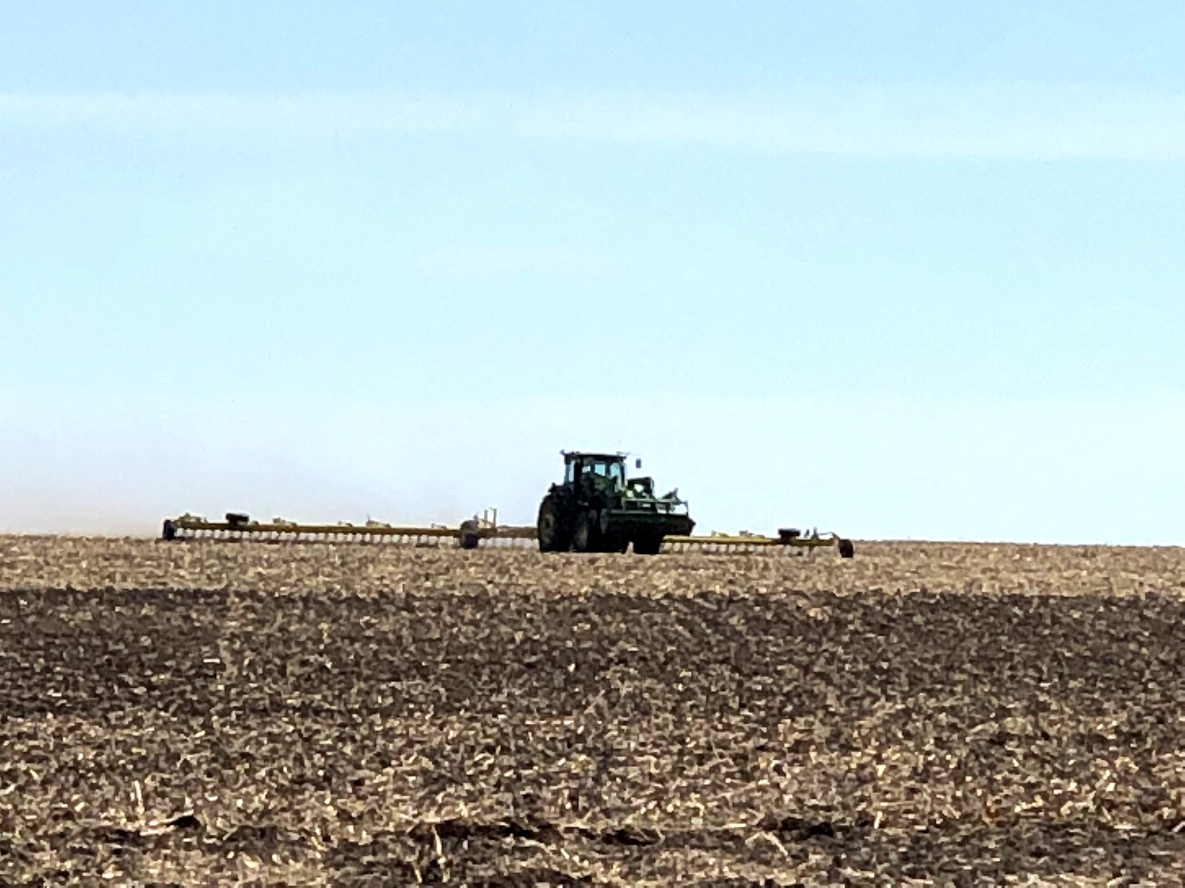 A John Deere tractor pulling heavy harrows on open ground