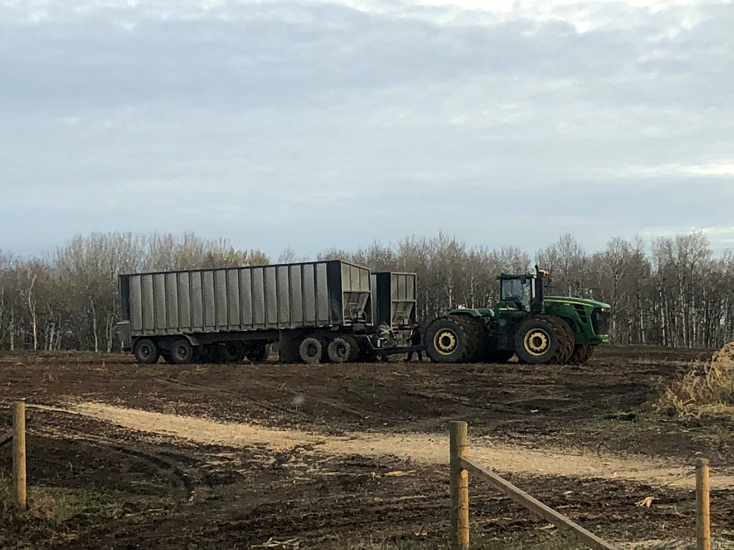 A John Deere four-wheel-drive tractor with a silage trailer at the field edge