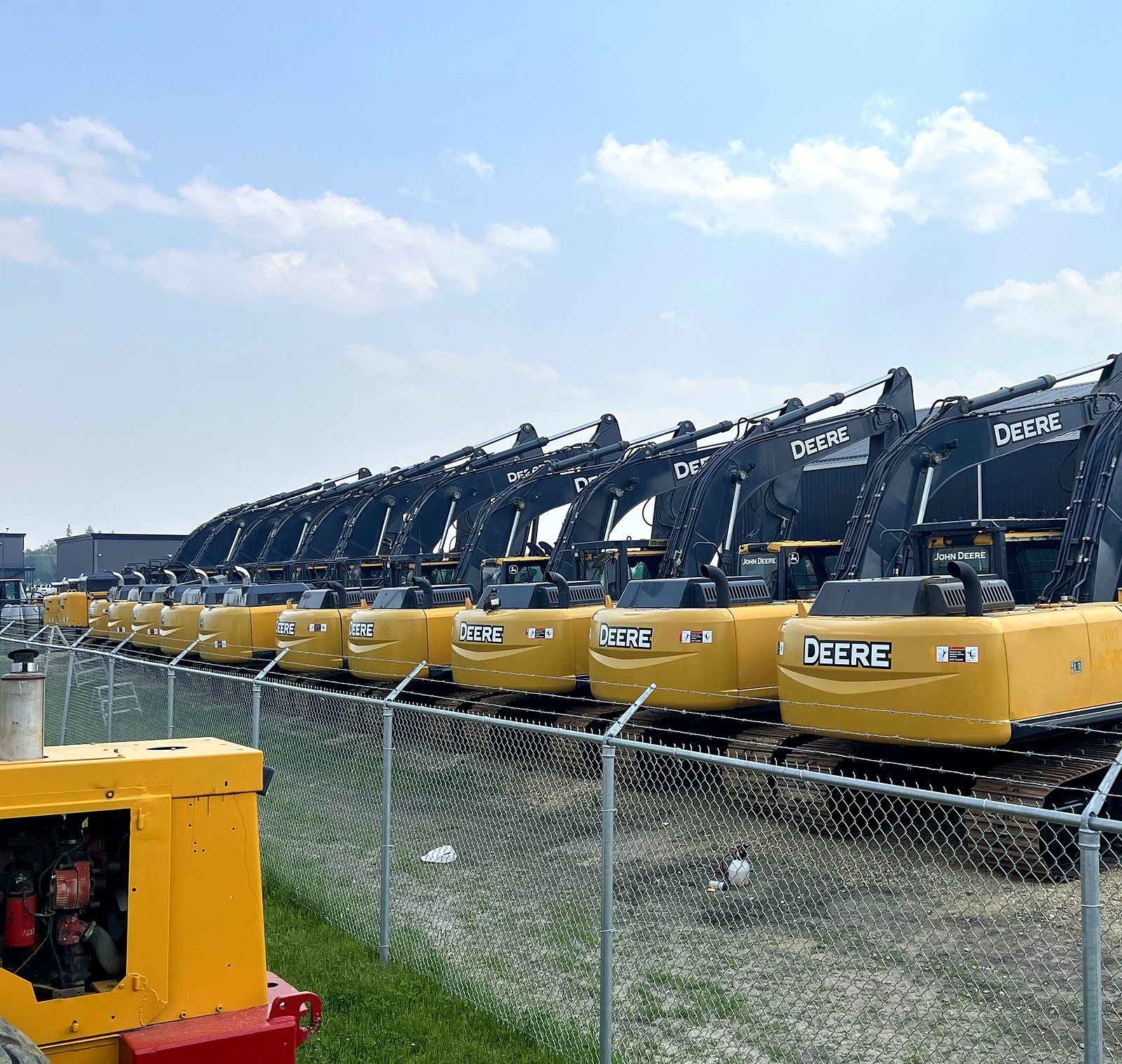 A row of John Deere excavators behind the yard fence