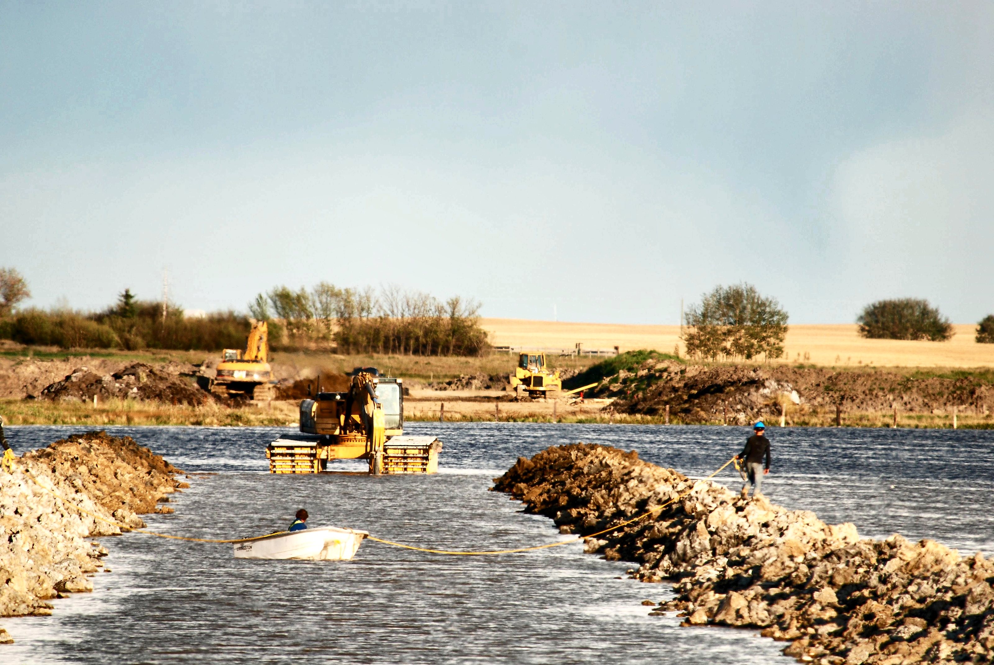 A crew closing two rock causeways across open water at Weed Lake, Alberta