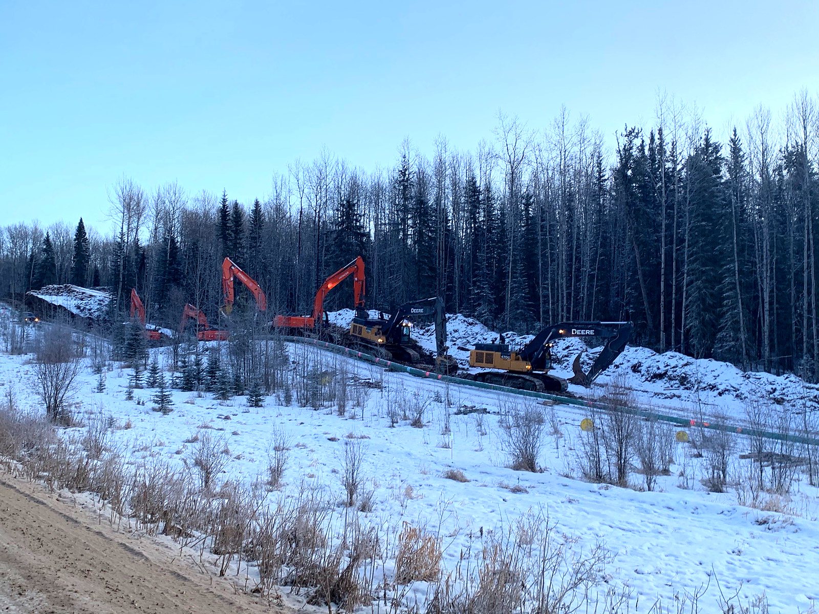 Excavators at work on a winter right-of-way at dusk
