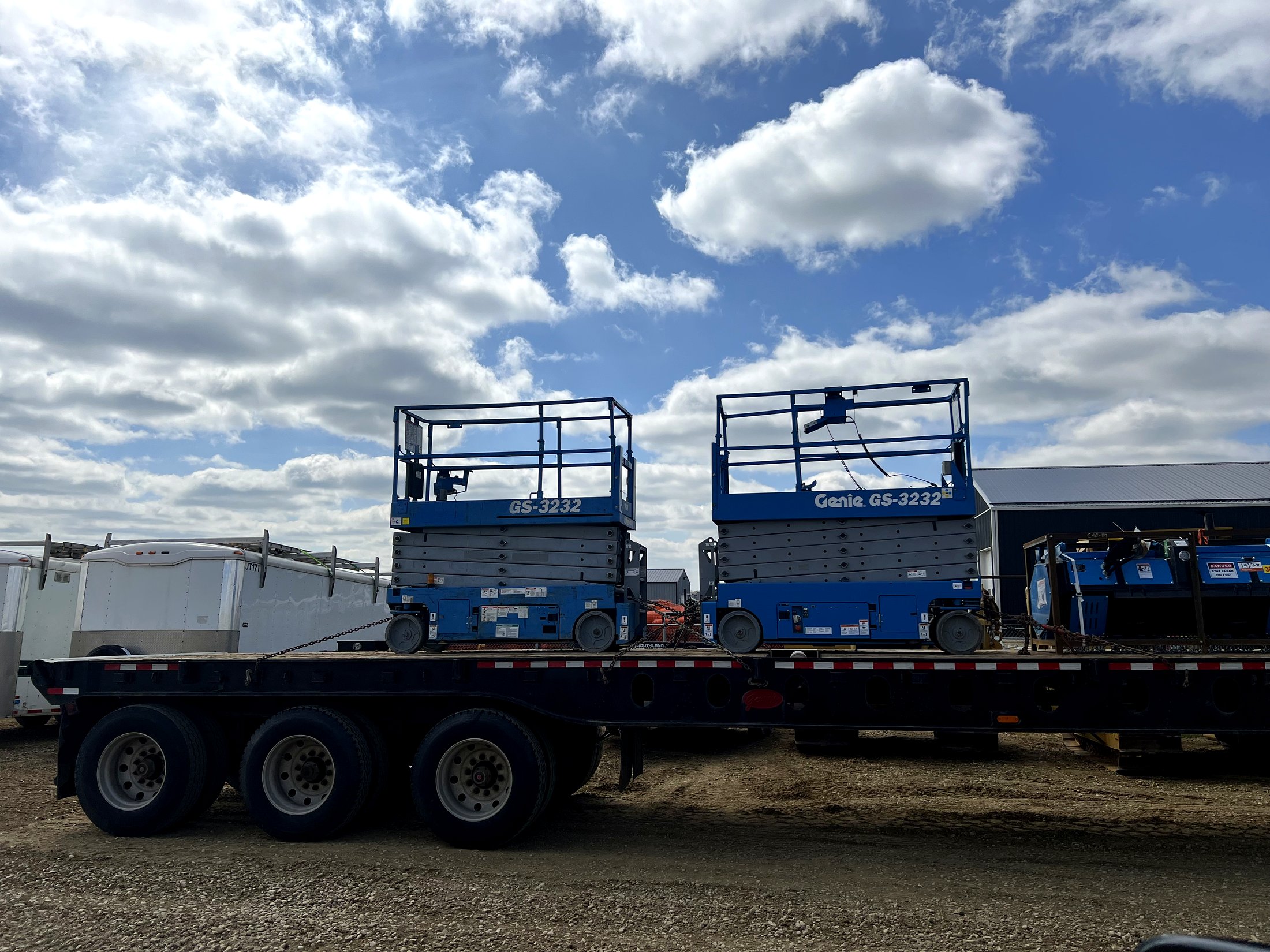 Two Genie GS-3232 scissor lifts loaded on a flatbed trailer
